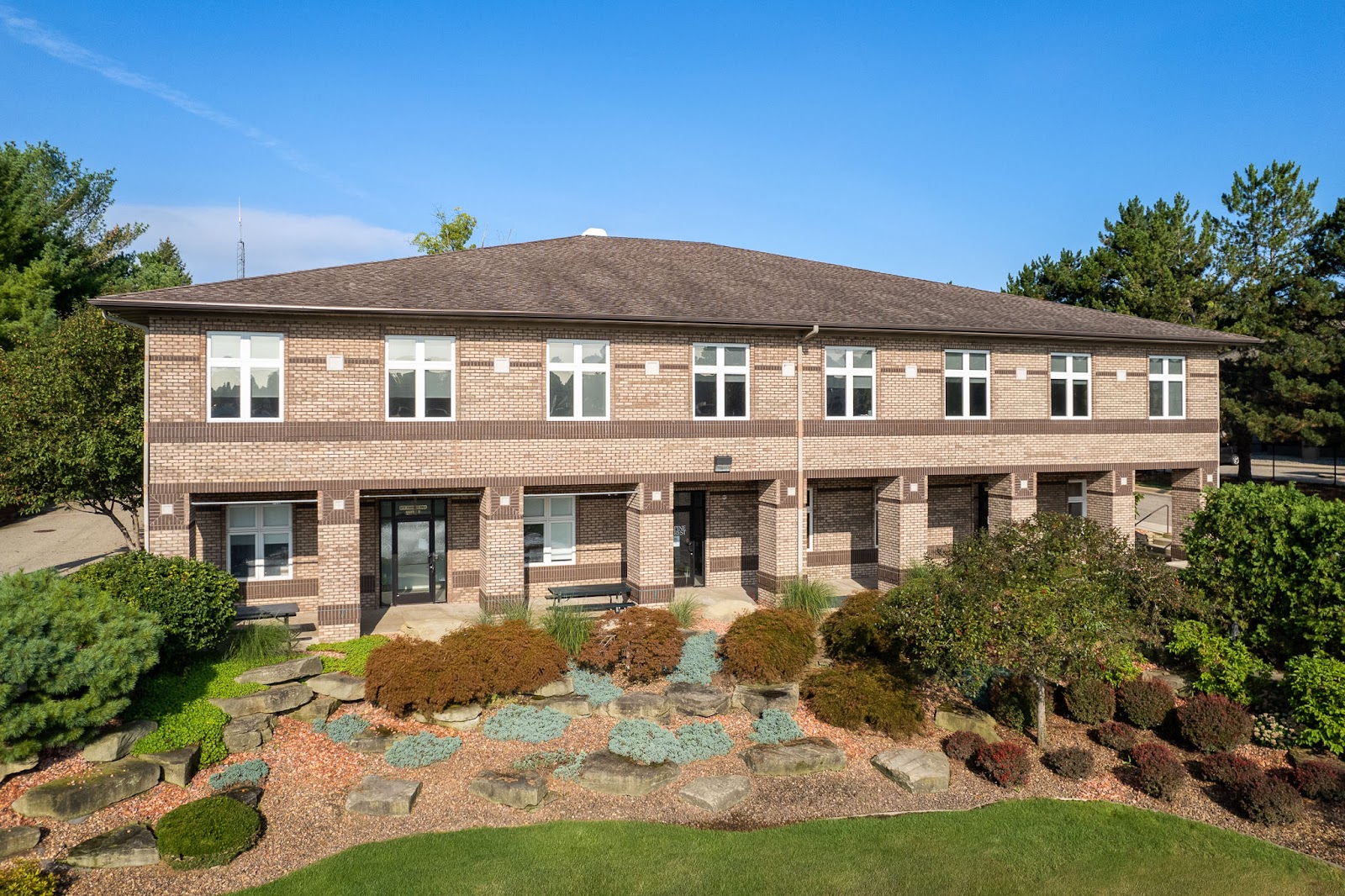 Multi-story brick building exterior with entrance doors, decorative landscaping, and manicured grounds