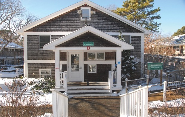 Exterior view of two-story gray shingled building with white trim, covered entrance portico, and landscaping