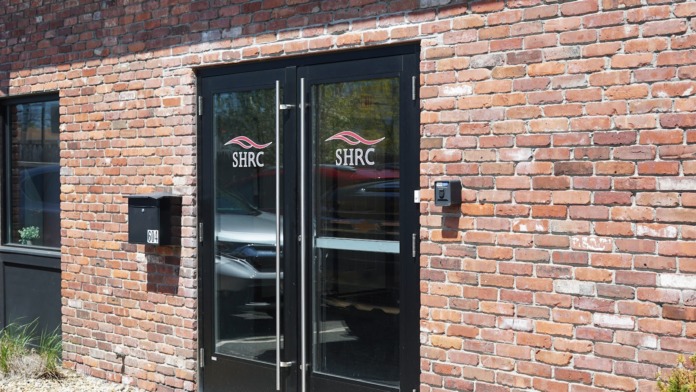 Exterior entrance showing double glass doors with SHRC branding and brick building facade