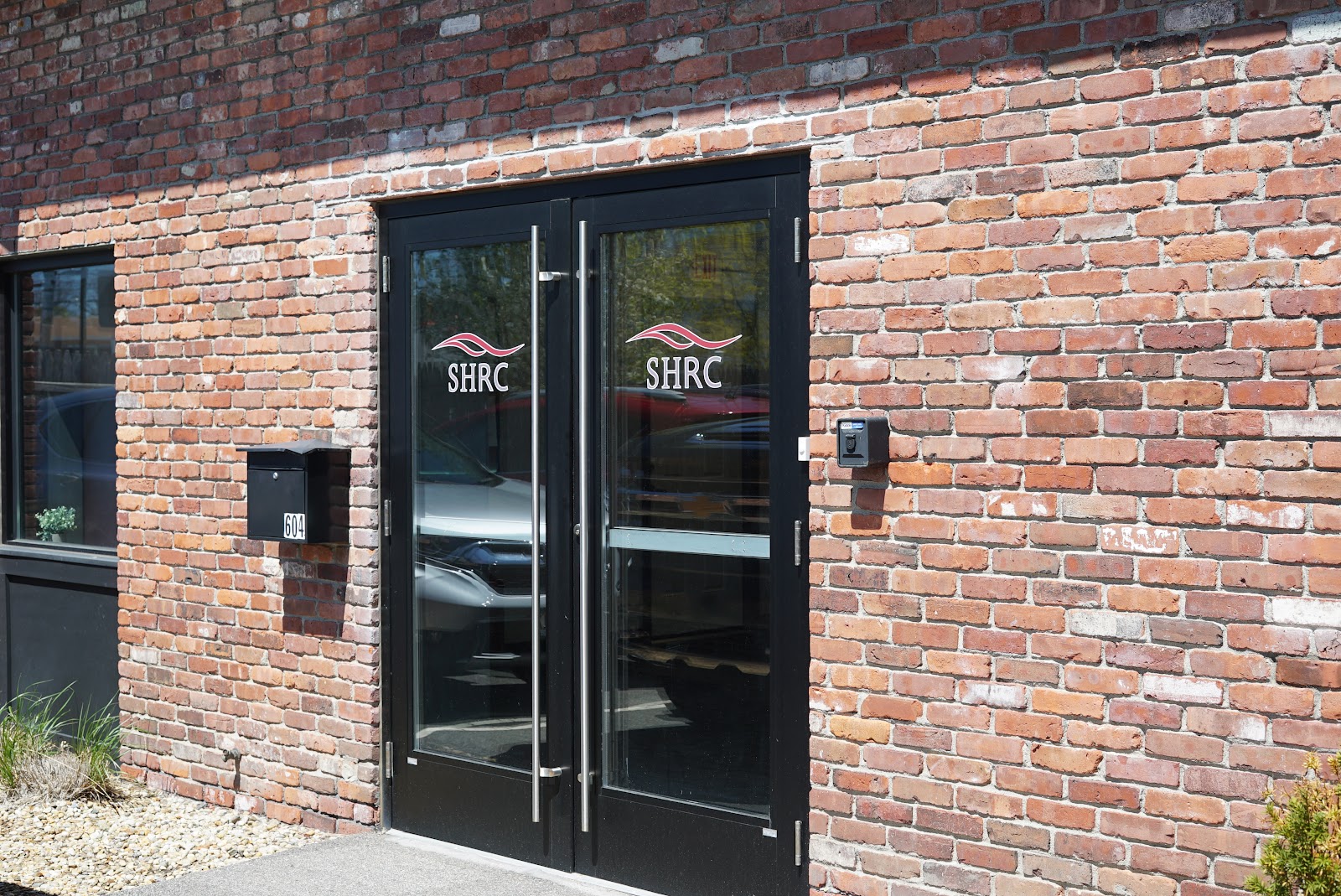 Exterior entrance showing double glass doors with SHRC branding and brick building facade