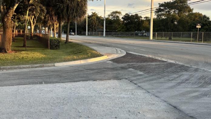 Exterior street view of facility driveway with mature trees, landscaping, and access road