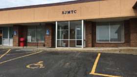 Exterior view of treatment center building with brick facade, main entrance doors, windows, and parking lot with handicap spaces