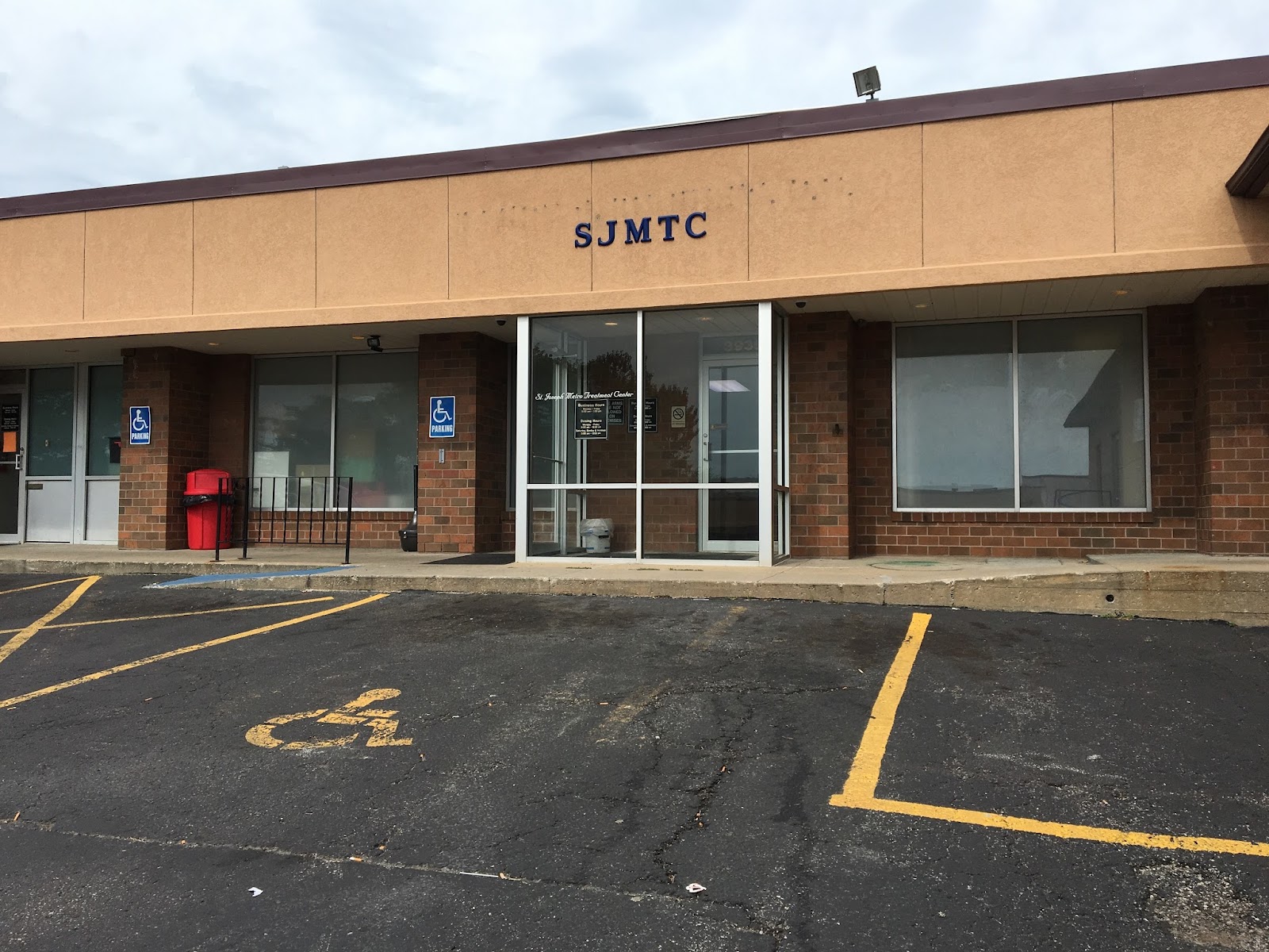 Exterior view of treatment center building with brick facade, main entrance doors, windows, and parking lot with handicap spaces