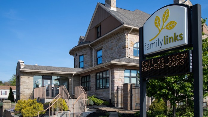 Exterior close-up of entrance with FamilyLinks logo sign, metal railings, stone facade, and landscaping