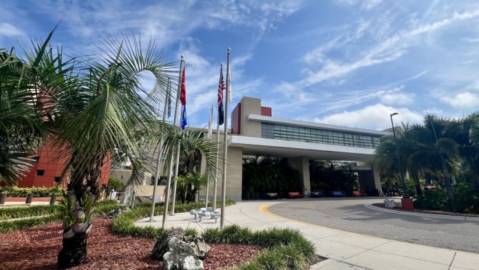 Exterior view of hospital entrance with palm trees, clear sky, and landscaped grounds