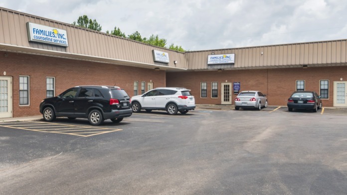 Exterior view of brick treatment facility with Families, Inc. counseling services signage, parking lot with vehicles, and metal roof structure