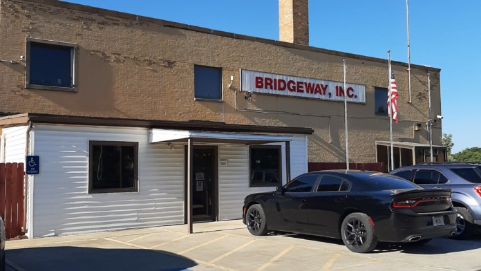 Exterior facility entrance showing accessible parking space, white entrance vestibule, brick building, flagpole, and parking area