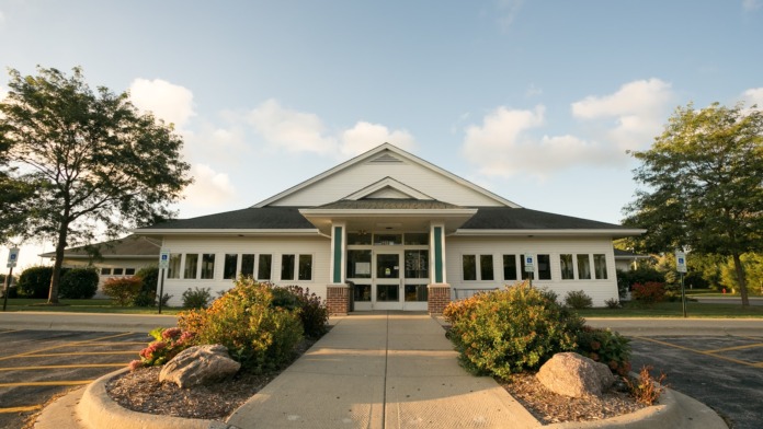 Exterior front entrance with symmetrical landscaping, brick pedestrian pathway, gabled entrance portico, and facility entrance doors