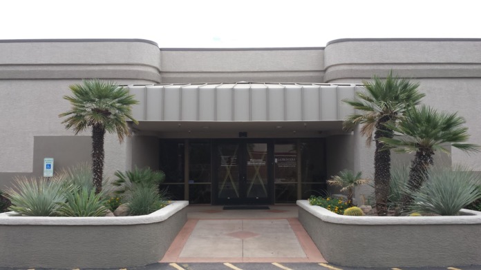 Exterior front entrance with decorative landscaping, palm trees, and facility entrance door