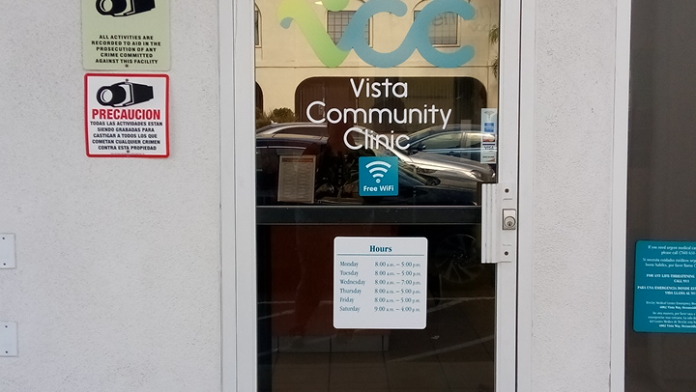 Exterior entrance doors with metal railing, facility signage, and operational information displayed on glass