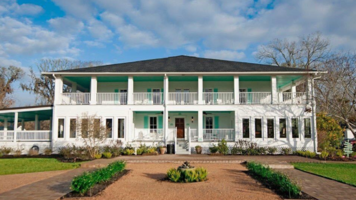 Exterior front entrance with circular brick driveway, columned entry portico, manicured landscaping, and mature trees