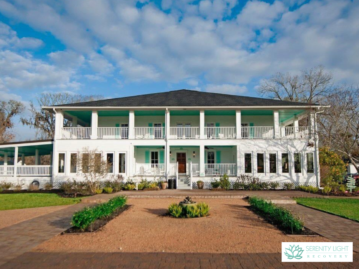 Exterior front entrance with circular brick driveway, columned entry portico, manicured landscaping, and mature trees