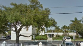 Exterior view of Henderson Behavioral Health facility showing white building with metal fencing, landscaping, and parking area with vehicles