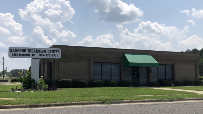 Exterior view of Sanford Treatment Center building with facility name sign, green awning, landscaping, and parking area