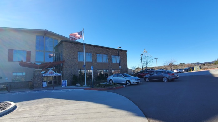 Exterior view showing modern healthcare facility with mixed facade materials, vehicles, and grounds