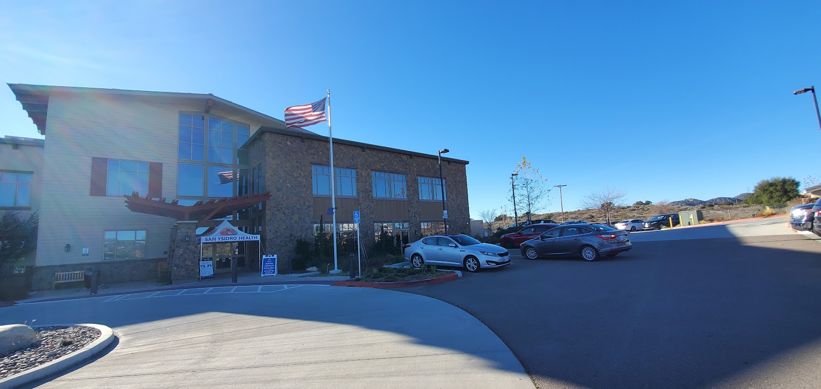Exterior view showing modern healthcare facility with mixed facade materials, vehicles, and grounds