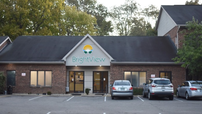 Exterior front view of brick facility with BrightView signage, gabled roof, windows, and parked vehicles at dusk.