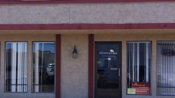 Exterior showing facility entrance with glass door, windows with blinds, tan stucco walls, and red structural framing