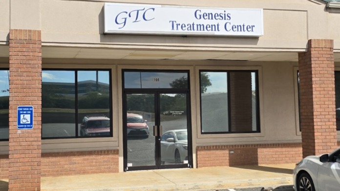 Exterior view of treatment center showing full front facade with signage, entrance doors, parking spaces, and landscaped roofline