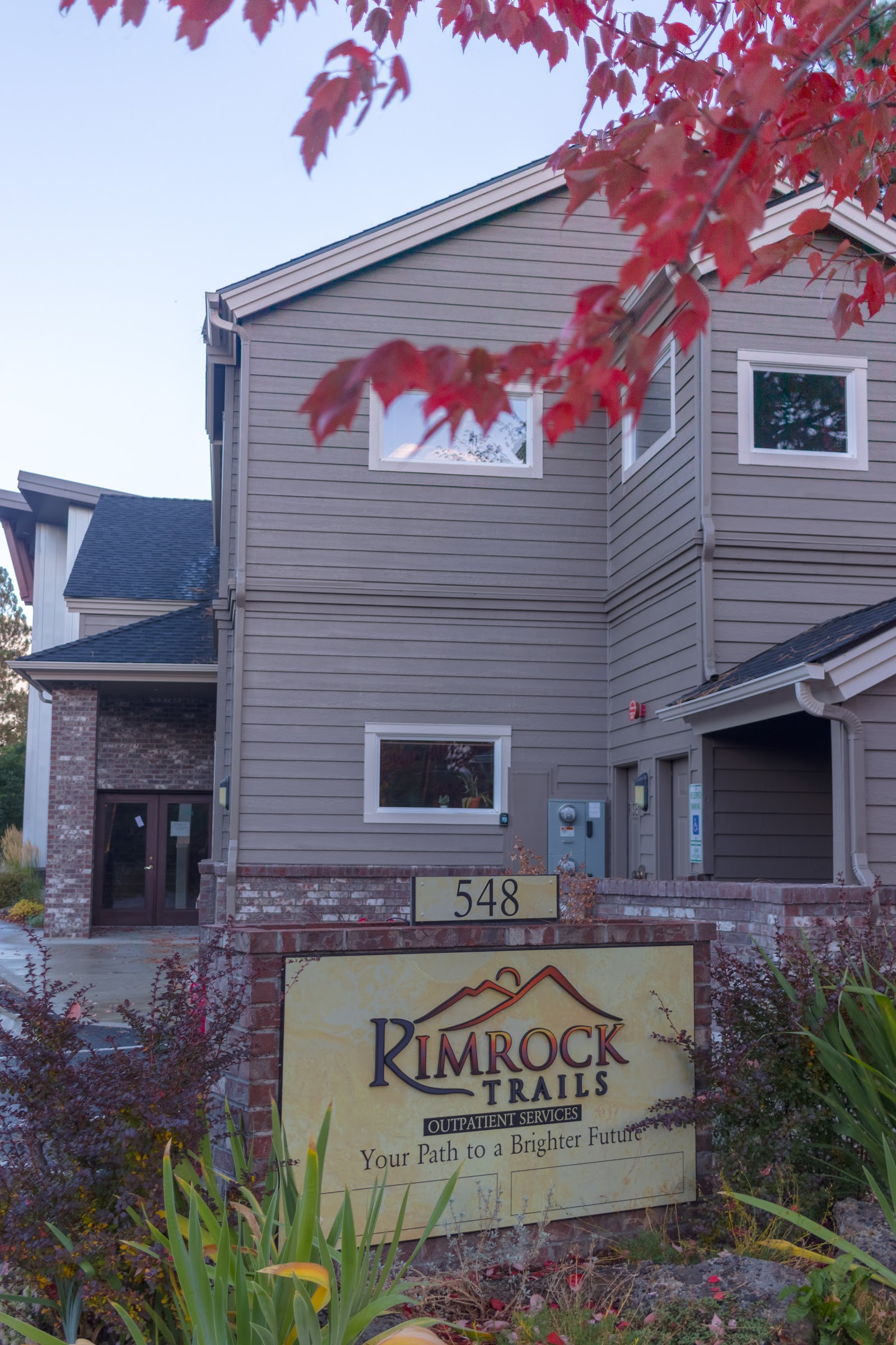 Exterior front facade of treatment facility building with red maple leaves overhead, signage, and landscaped grounds.