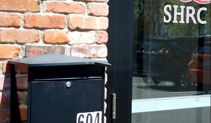 Exterior view of double glass entrance doors with SHRC logo decals and welcome information posted