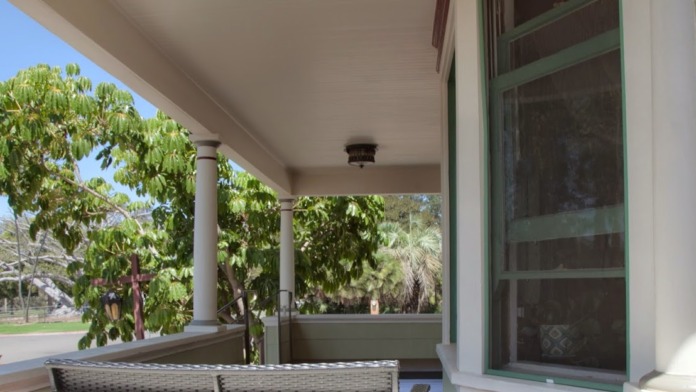 Exterior porch view showing covered entry with columns, green landscaping, and clear sightline to street and park area