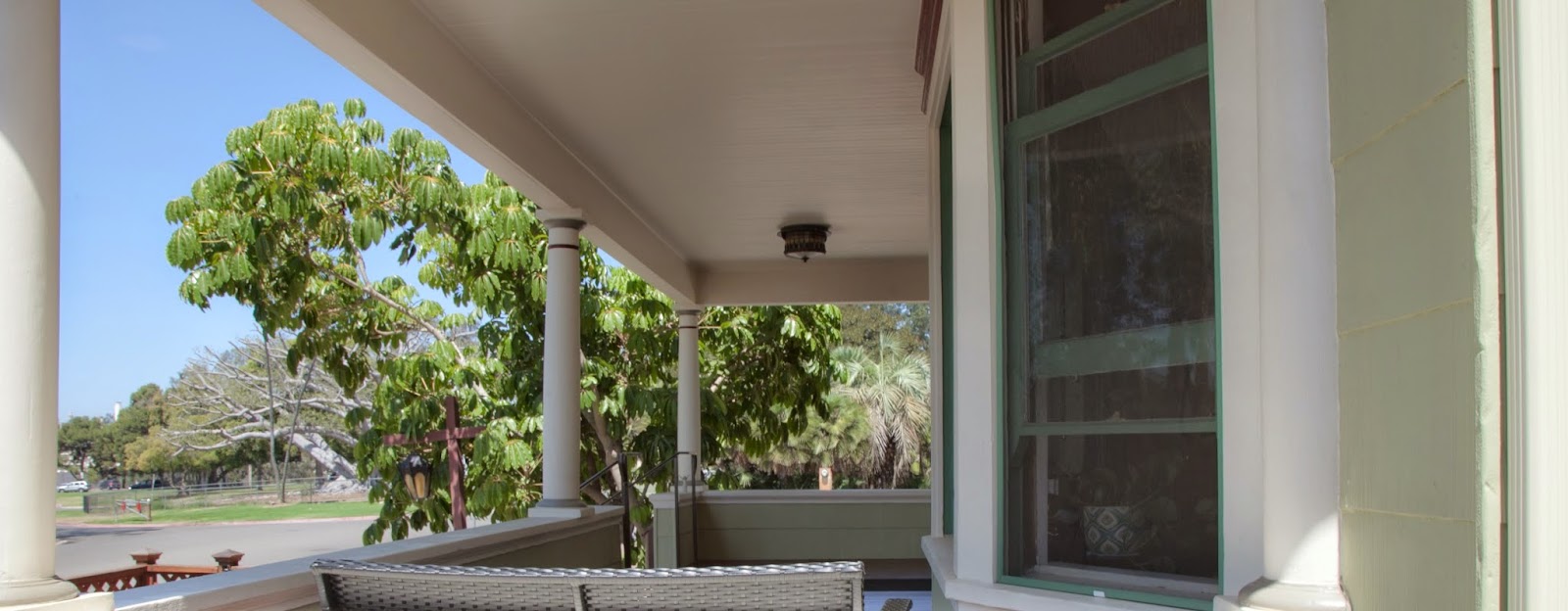 Exterior porch view showing covered entry with columns, green landscaping, and clear sightline to street and park area
