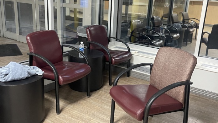 Interior glass-walled room with burgundy and tan seating, side tables, and view of exterior common area