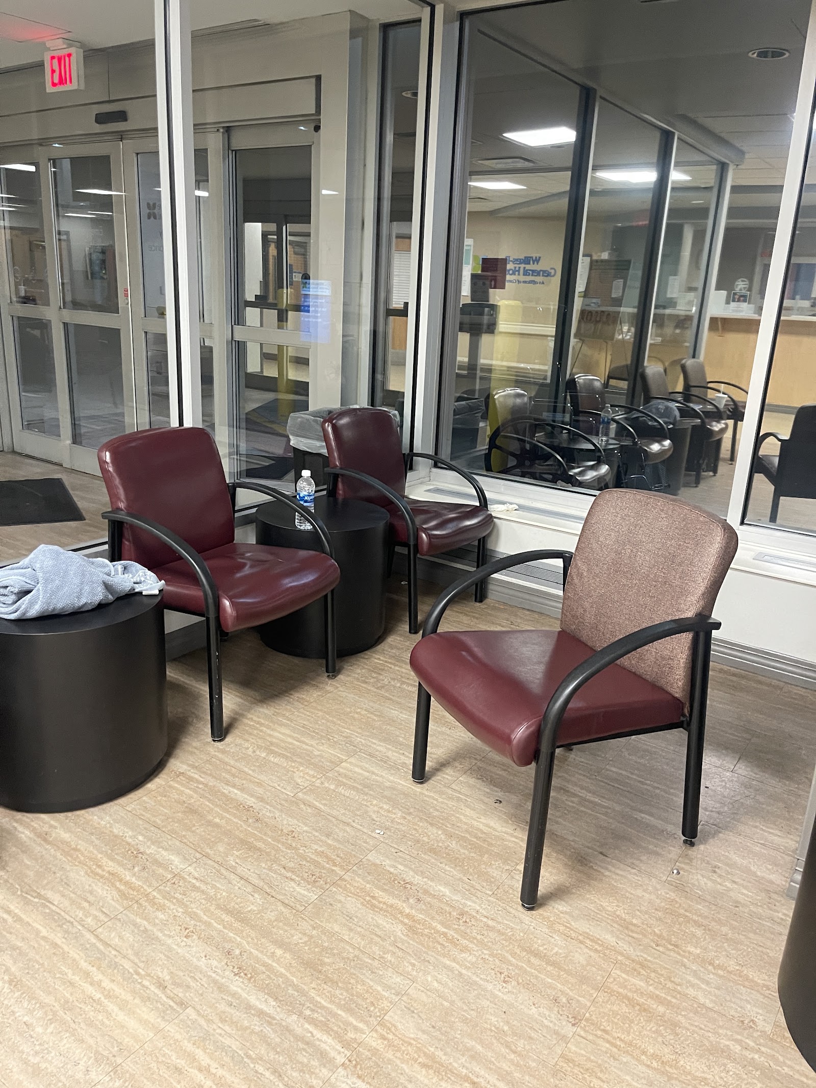 Interior glass-walled room with burgundy and tan seating, side tables, and view of exterior common area