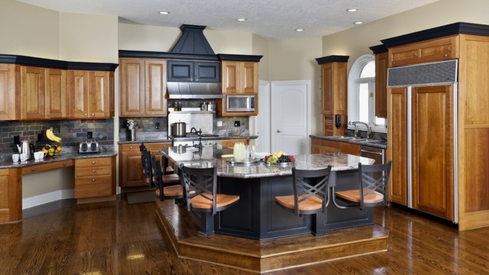 Interior gourmet kitchen featuring wood cabinetry, black island, stainless steel appliances, and dining seating for communal meals