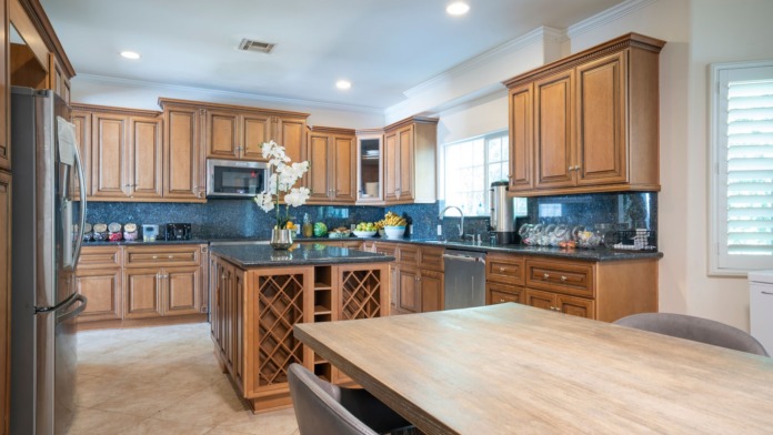 Interior modern kitchen with wood cabinetry, blue tile backsplash, stainless appliances, and large island counter