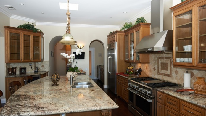 Interior chef's kitchen featuring large granite island, stainless steel appliances, wood cabinetry, pendant lighting, and professional cooking amenities