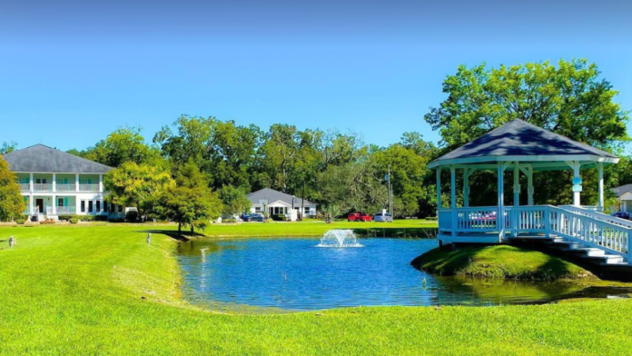 Exterior grounds featuring blue gazebo, pond with fountain, mature trees, green lawn, and facility building in background
