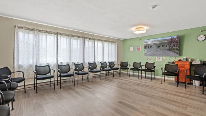 Interior activity or waiting room with pale green walls, rows of black armchairs with white trim, large windows, wall art, and flooring