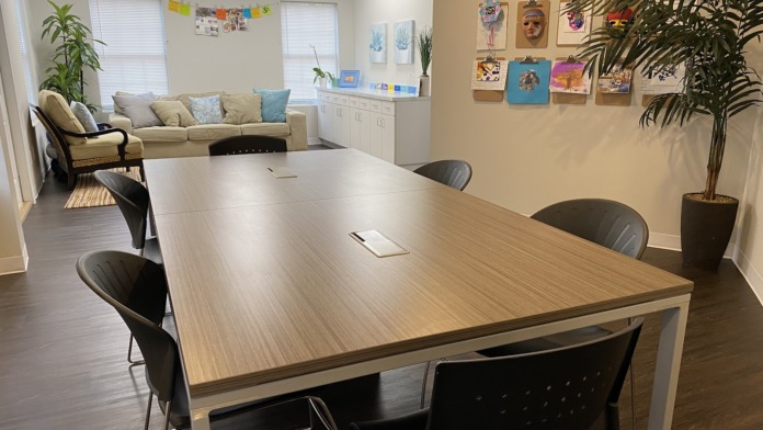 Interior activity room with large table, multiple chairs, windows, wall art, plants, and natural lighting