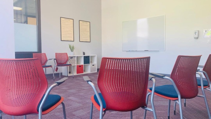 Interior meeting space with red perforated chairs, whiteboard, storage shelving, and modern furnishings