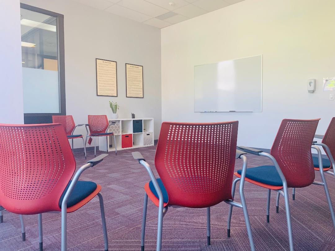 Interior meeting space with red perforated chairs, whiteboard, storage shelving, and modern furnishings