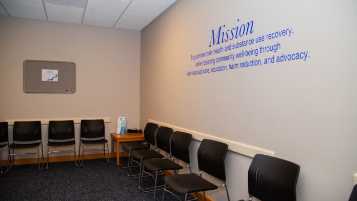 Interior meeting room with multiple black chairs arranged in rows, mission statement displayed on wall, cork board, and motivational signage