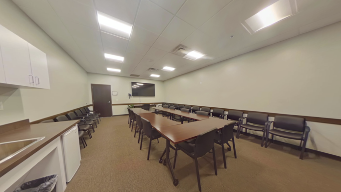 Interior conference room with large conference table, multiple chairs arranged in U-shape, whiteboard, and presentation screen