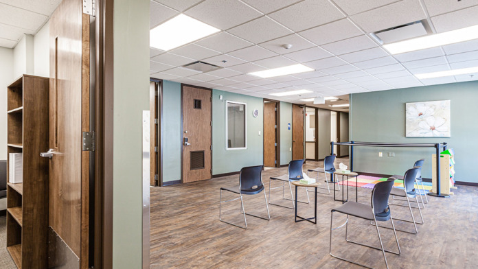 Interior group meeting room with blue stackable chairs, wood flooring, glass partitions, and modern fixtures