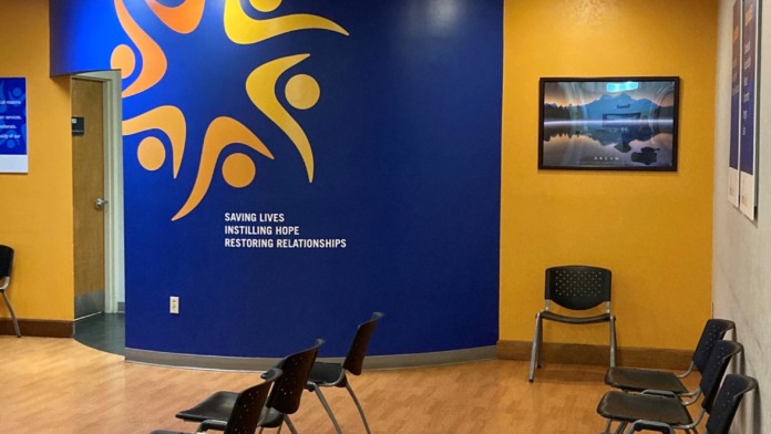 Interior activity space with blue accent wall, facility mission statement, yellow walls, chairs arranged for group sessions, and calm environment