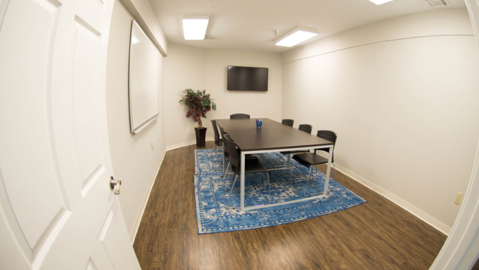 Interior group therapy room with conference table, chairs, whiteboard, television, and plants