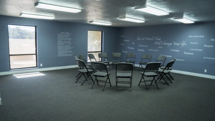 Interior meeting room with circle of black folding chairs, blue walls with inspirational text, and large windows