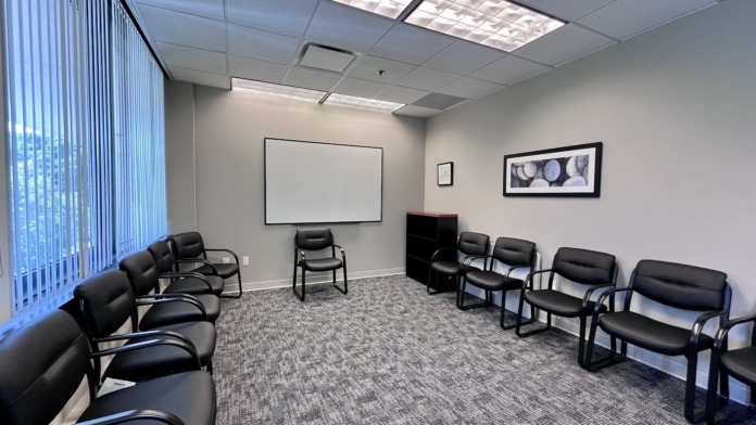 Interior therapy room with multiple black chairs arranged in rows, projection screen, and window with blinds