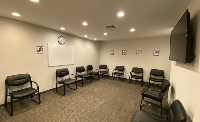 Interior group therapy space with multiple black padded chairs arranged in semi-circle with wall clock and whiteboard