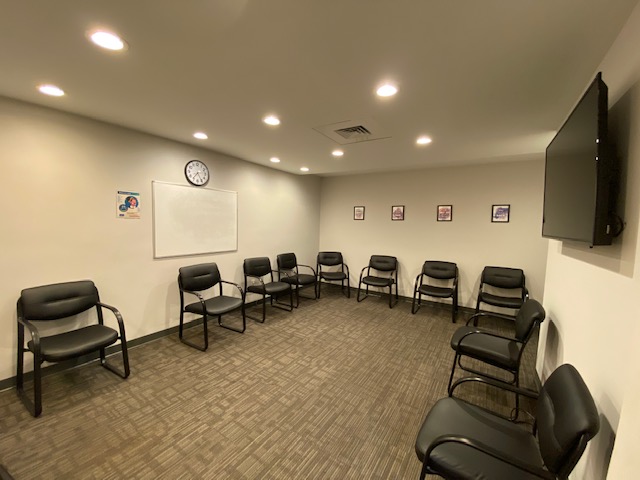 Interior group therapy space with multiple black padded chairs arranged in semi-circle with wall clock and whiteboard