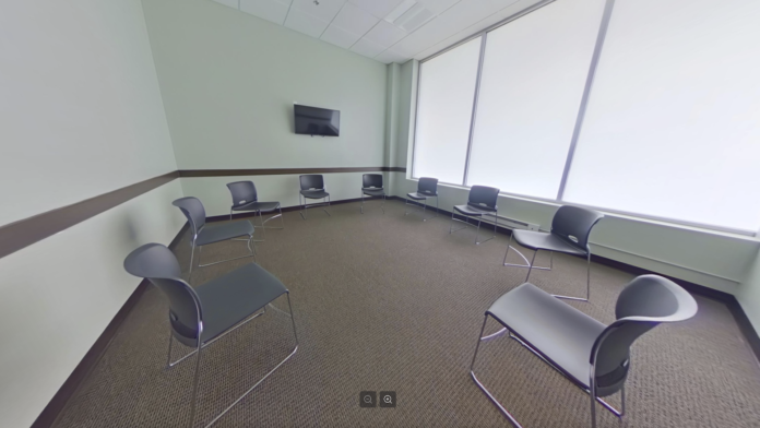 Interior group therapy room with chairs arranged in circle, mounted television, light green walls with wood trim