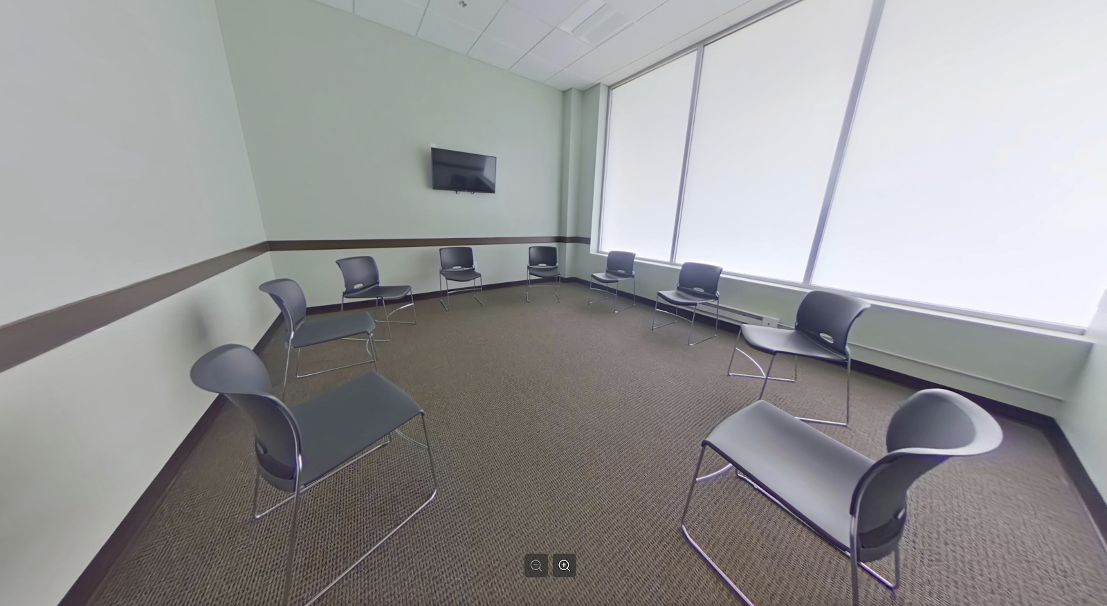 Interior group therapy room with chairs arranged in circle, mounted television, light green walls with wood trim