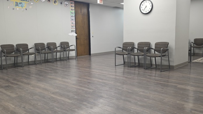 Interior group therapy space with multiple gray mesh chairs arranged in rows, wall decorations, and clock