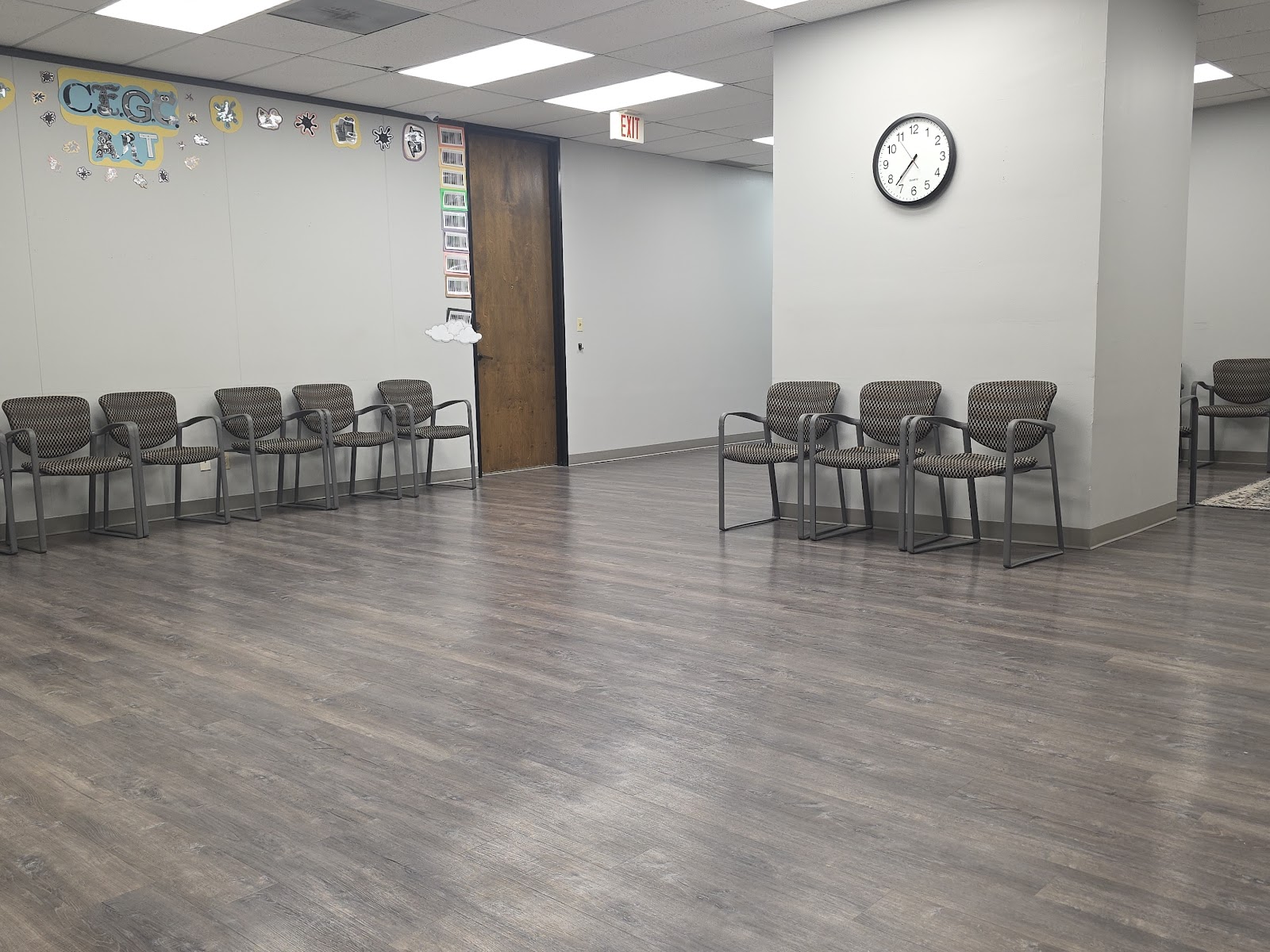 Interior group therapy space with multiple gray mesh chairs arranged in rows, wall decorations, and clock